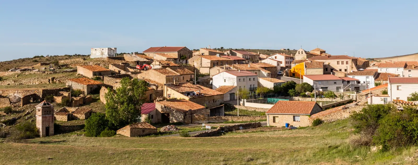 Panoramic view of Anquela del Pedregal, with stone houses and the church among meadows.