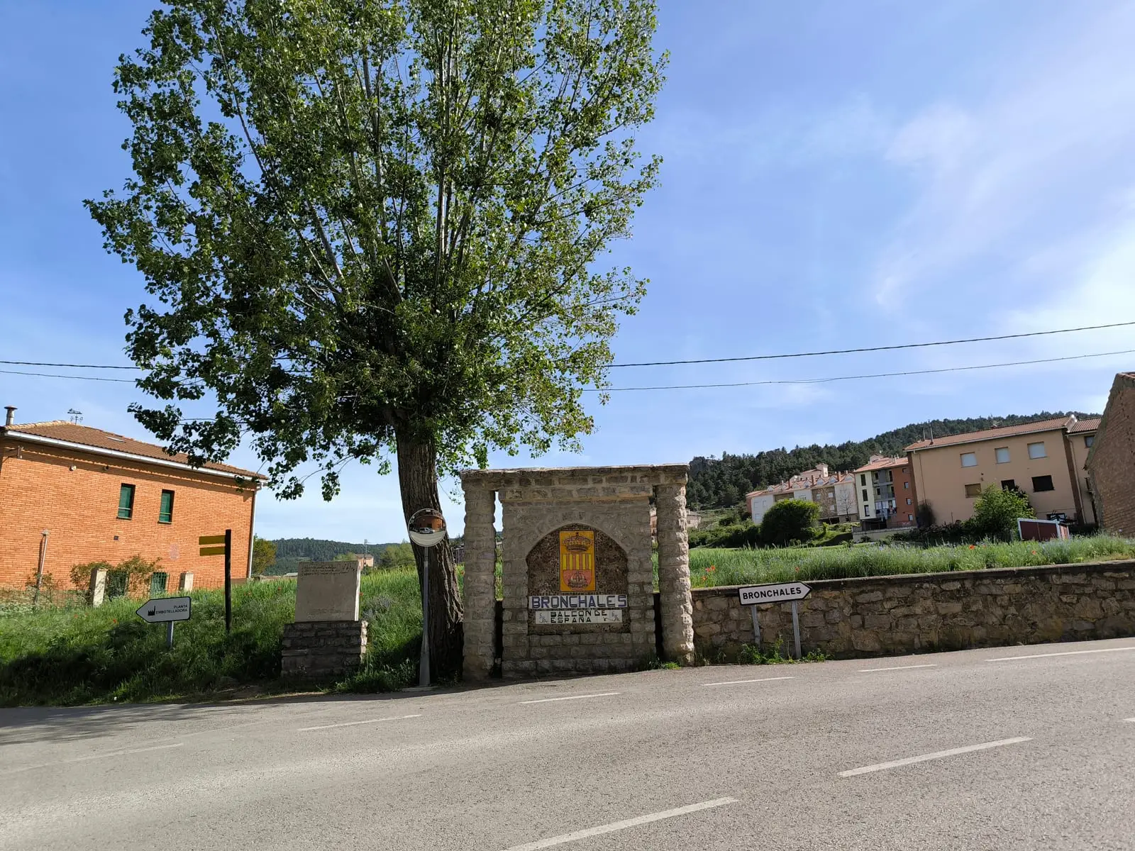 Rótulo de piedra que da la bienvenida a Bronchales, junto a casas del núcleo y el arbolado de la sierra.