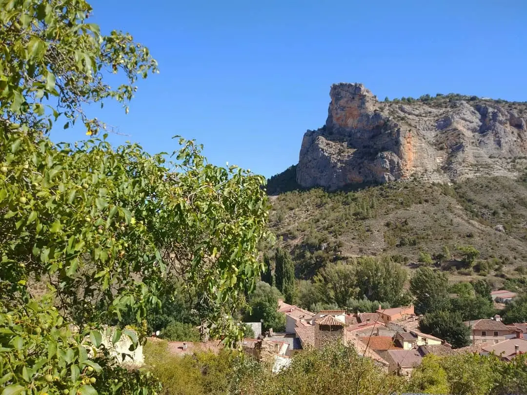 Huertapelayo’s houses at the foot of a rock wall, seen through trees.