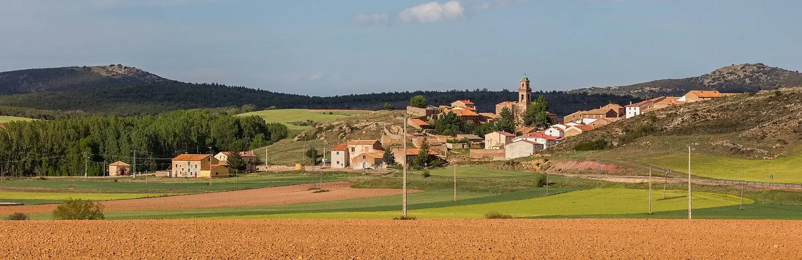 Panoramic view of Setiles with the church and village houses among fields and hills.