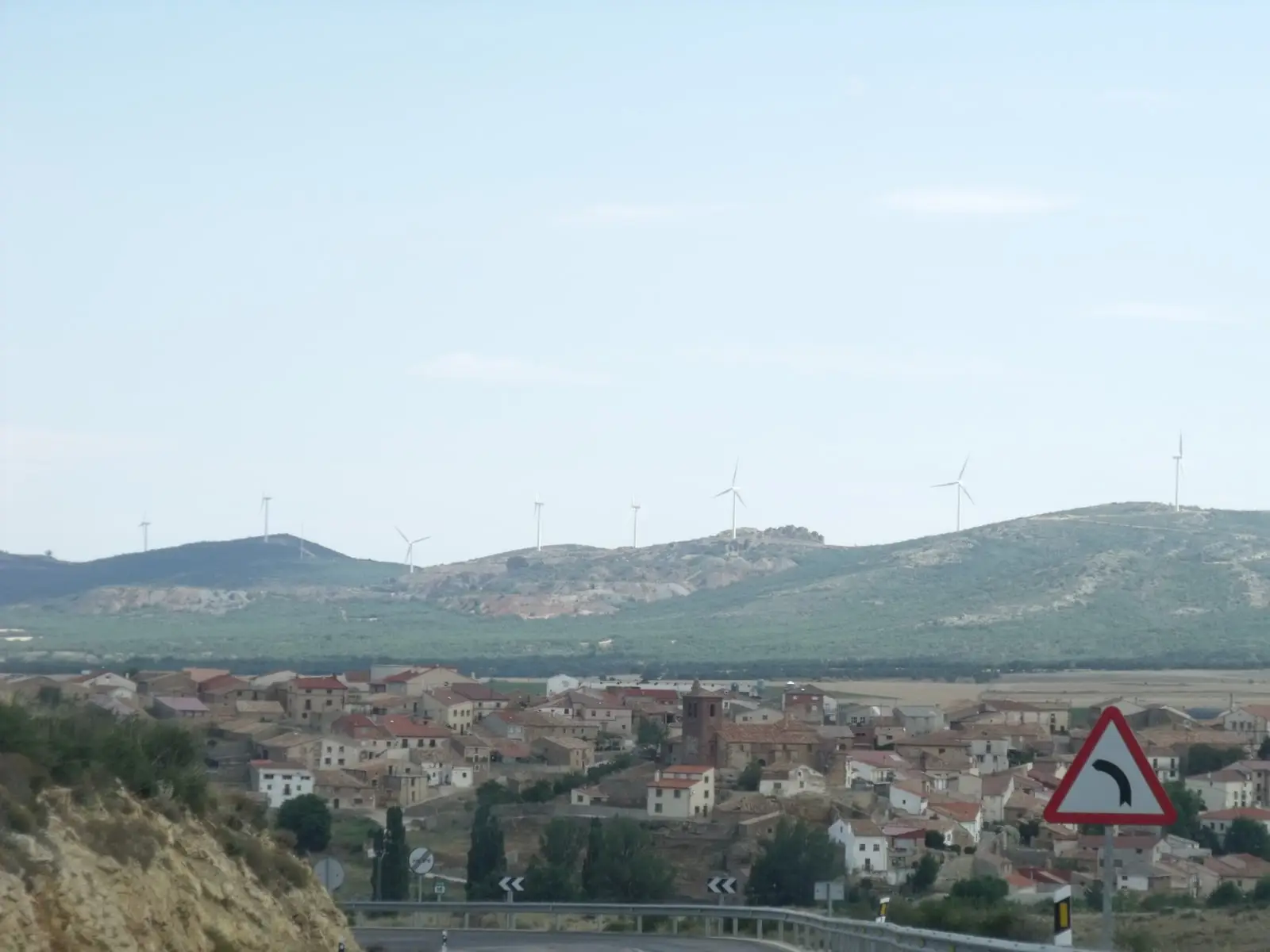 General view of Tordesilos, with houses below hills bearing wind turbines.