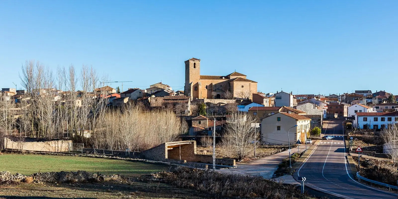 Panoramic view of Tortuera with its church and village houses beside fields and trees.